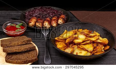 Roasted Potato In The Pot, Pieces Of Rye Black Bread On A Wooden Serving Plate, Homemade Sausages In