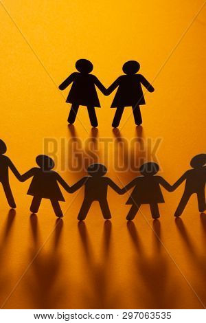 Black paper figure of a female couple in front of a crowd of paper people holding hands on orange background. Social movement, minorities, same-sex marriage concept.