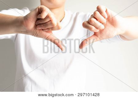 Woman In White T-shirt Showing Two Hands With Thumbs Down On White Background; Gesturing Negative Si