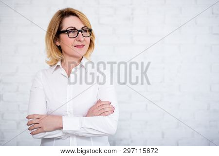 Portrait Of Mature Business Woman In Eyeglasses Posing Over White Brick Wall With Copy Space
