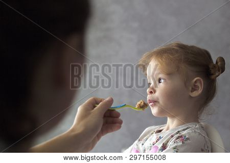 Mother Feeds Her Daughter With A Small Spoon, Mother Gives Healthy Food To Her Red-haired Little Gir