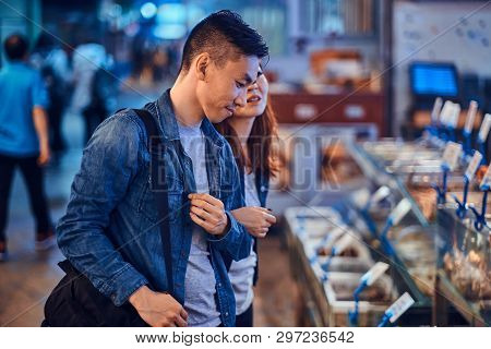 Young Asian Couple Looking For Something Special At Traditional Chainese Market. They Are Pensive. A