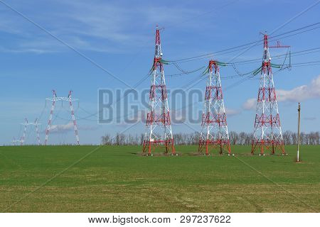 Supports Power Lines Are In The Field. Red And White Against A Bright Blue Sky. Solar Panels For Nig