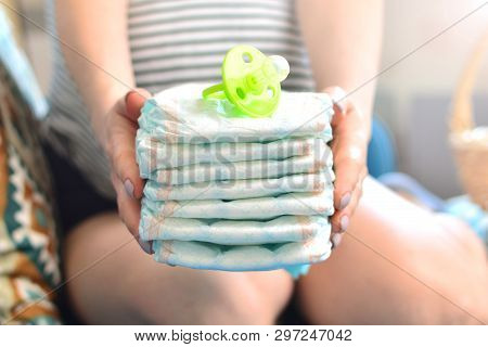 Stack Of Diapers And Soother In The Hands Of A Pregnant Woman
