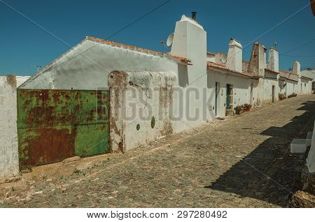 Humble White Wall Houses With Iron Garage Gate In A Sunny Day, On The Cobblestone Main Street Of Evo