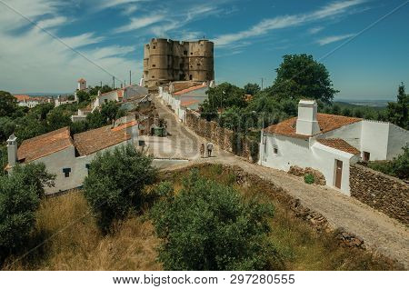 People Walking Up The Main Cobblestone Street In A Sunny Day Towards The Castle Of Evoramonte. A Tin