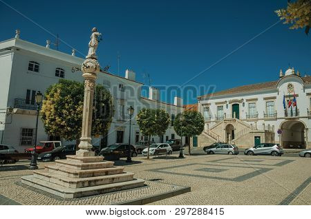 Marble Pillory With Sculpture In Square, Old Buildings And City Hall In The Back, In A Sunny Day At 