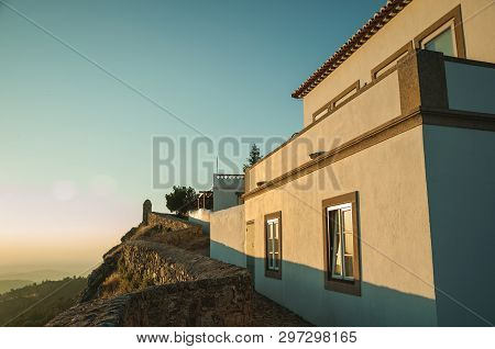 Stone Wall And Old Whitewashed House Over Rocky Cliff, With Hilly Landscape And Sunset Glow At Marva