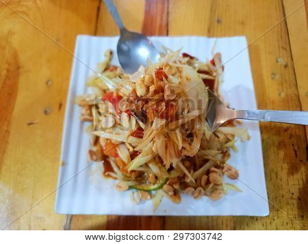 Selective Focus Of Papaya Salad In Spoon On Blurred Papaya Salad In White Plate In Restaurant, Som T