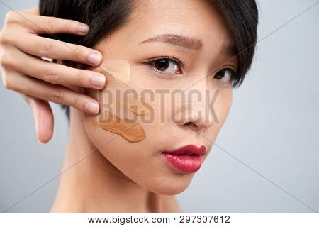 Portrait Of Young Vietnamese Woman Applying Foundation Swatches Of Various Tones On Her Face