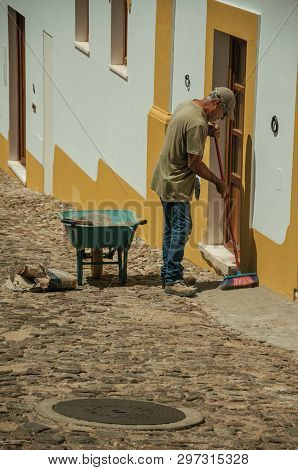 Evoramonte, Portugal - July 6, 2018. Man sweeping the front of colorful house at the main street of Evoramonte. A tiny fortified civil parish over hill where stands out its historic castle in Portugal