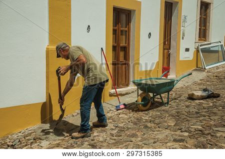 Evoramonte, Portugal - July 6, 2018. Mason working in front of colorful house at the main street of Evoramonte. A tiny fortified civil parish over hill where stands out its historic castle in Portugal