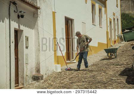 Evoramonte, Portugal - July 6, 2018. Mason working in front of colorful house at the main street of Evoramonte. A tiny fortified civil parish over hill where stands out its historic castle in Portugal