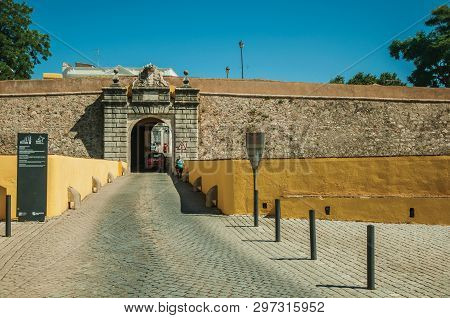 Elvas, Portugal - July 07, 2018. Woman walking a street going toward a city wall gateway, in a sunny day at Elvas. A gracious star-shaped fortress city on the easternmost frontier of Portugal.