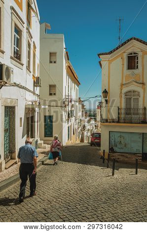 Elvas, Portugal - July 07, 2018. Street with colorful old houses in a narrow causeway and elders walking at Elvas. A gracious star-shaped fortress city on the easternmost frontier of Portugal.