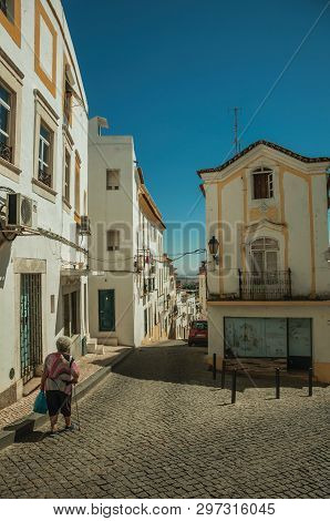 Elvas, Portugal - July 07, 2018. Street with colorful old houses in a narrow causeway and elders walking at Elvas. A gracious star-shaped fortress city on the easternmost frontier of Portugal.
