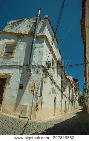 Elvas, Portugal - July 7, 2018. Old white houses with peeling plaster and deserted causeway in a narrow alley at Elvas. A gracious star-shaped fortress city on the easternmost frontier of Portugal.