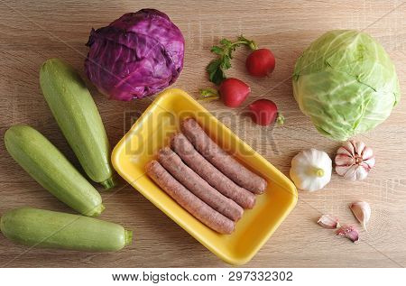 Raw Meat Sausages Kupaty And Vegetables - Cabbage, Zucchini, Radish And Garlic On Wooden Background 
