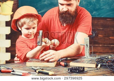 Father With Beard Teaching Little Son To Use Tools, Hammering, Chalkboard On Background. Handyman Co