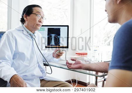 Senior Vietnamese Doctor Measuring Blood Preassure Of Young Patient