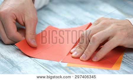 Man Creating Origami With Red Paper Close Up. Male Hands Dividing Paper Sheet In Half. Paper Folding