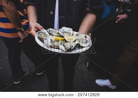 Man Hand Holding Fresh Raw Oyster In Paperr Plate With Lemon In Market.