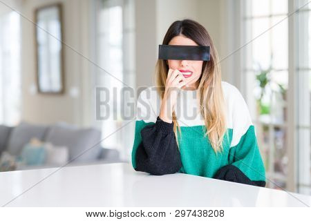 Young beautiful woman blindfold eyes with black censor band at home looking stressed and nervous with hands on mouth biting nails. Anxiety problem.