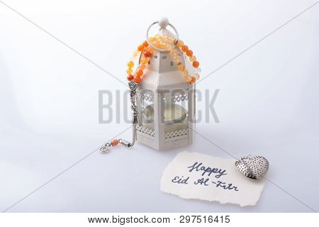 The Word Eid El Fitr   On Torn Paper Beside A Lantern And Prying Beads