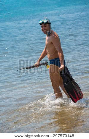 Young smiling fisherman with equipment standing in the shallow water of the sea while preparing for underwater fishing  active holiday concept