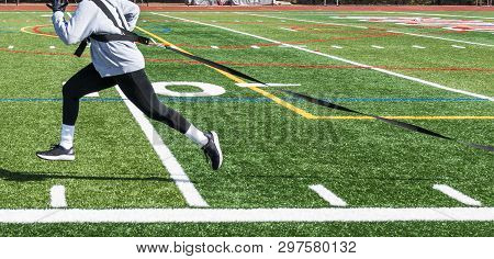 Female Pulling A Sled With Weight Across A Green Turf Field Wearing Black Spandex, Gray Sweatshirt A