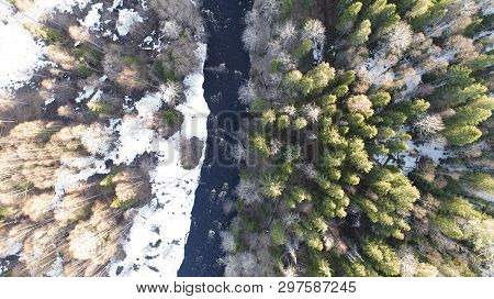Aerial View Of A River In The Forest With Snow Along The Banks.