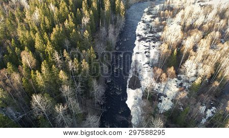 Aerial View Of A River In The Forest With Snow Along The Banks.