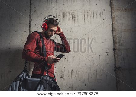 Muscular Athetic Man Wearing Sportswear And Carrying A Gym Bag, Listening To The Music And Using A S