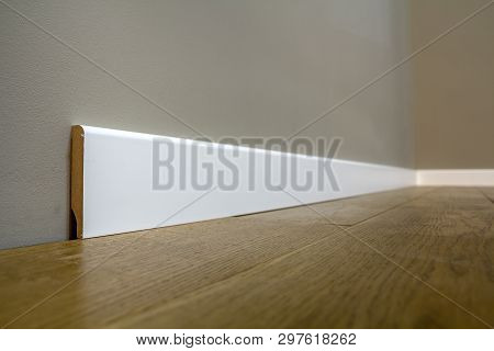 Wooden Or Plastic White Floor Plinth Installation In Big Empty Room On Wooden Floor And White Plaste