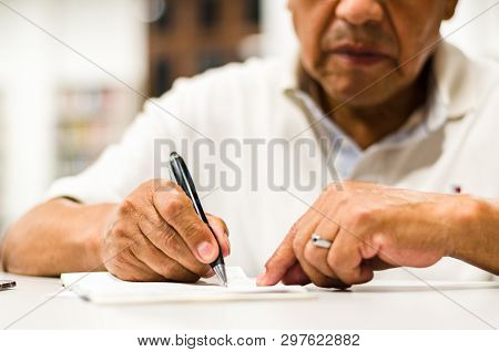 Serious Senior Man Sitting On A Library Bench Writing In His Book. Senior Man Sitting In A Universit