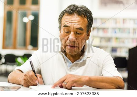 Serious Senior Man Sitting On A Library Bench Writing In His Book. Senior Man Sitting In A Universit
