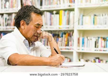 Serious Senior Man Sitting On A Library Bench, Writing In His Book. Senior Man Sitting In A Universi