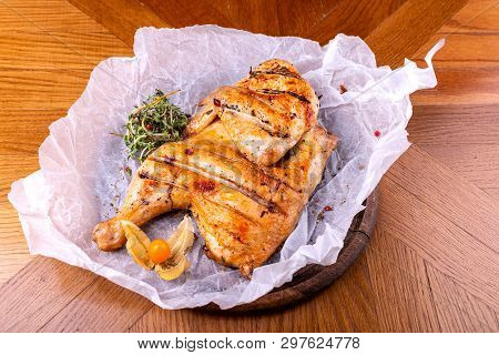 Grilled Chicken Tabaka Served With Herbs On Wooden Background