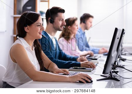Happy Young Customer Service Executives Using Earphones Working In Call Center