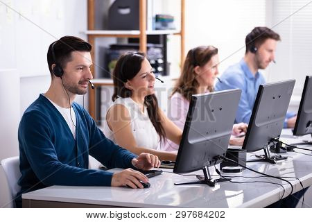 Happy Young Customer Service Executives Using Earphones Working In Call Center