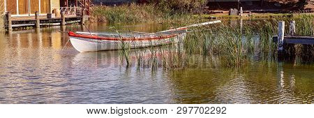 An Old Wooden Boat With Red Trim Floating Amongst Water Grass In A Calm Marina Recreated For Tourist