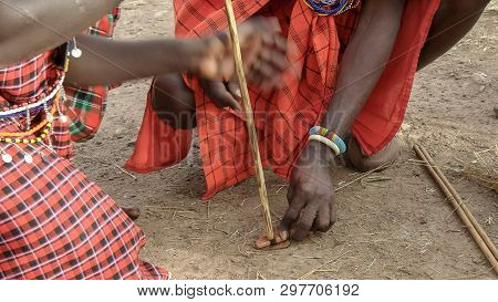Two Maasai Men Use A Hand Drill To Start A Fire At A Manyatta In Kenya