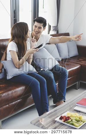 Happy Asian Young Couple Loving On The Couch Watching A Movie Together, Woman Holding Remote And Her