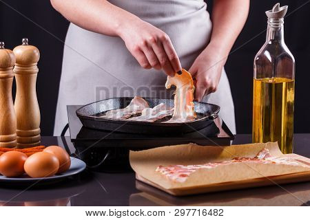 Young Woman In A Gray Apron Fries Bacon