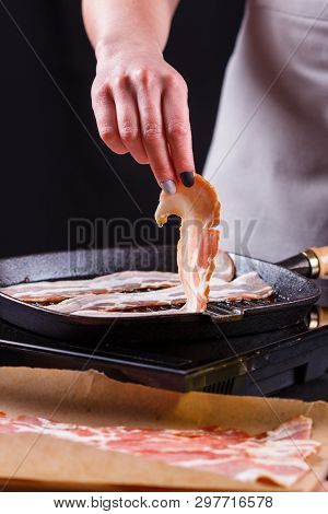 Young Woman In A Gray Apron Fries Bacon