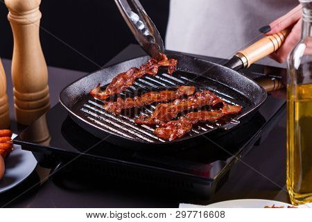 Young Woman In A Gray Apron Fries Bacon