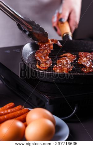 Young Woman In A Gray Apron Fries Bacon