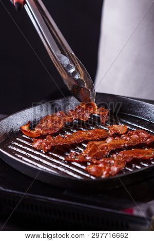 Young Woman In A Gray Apron Fries Bacon