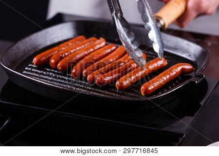 Young Woman In A Gray Apron Fries Sausages