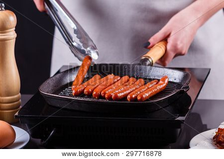 Young Woman In A Gray Apron Fries Sausages
